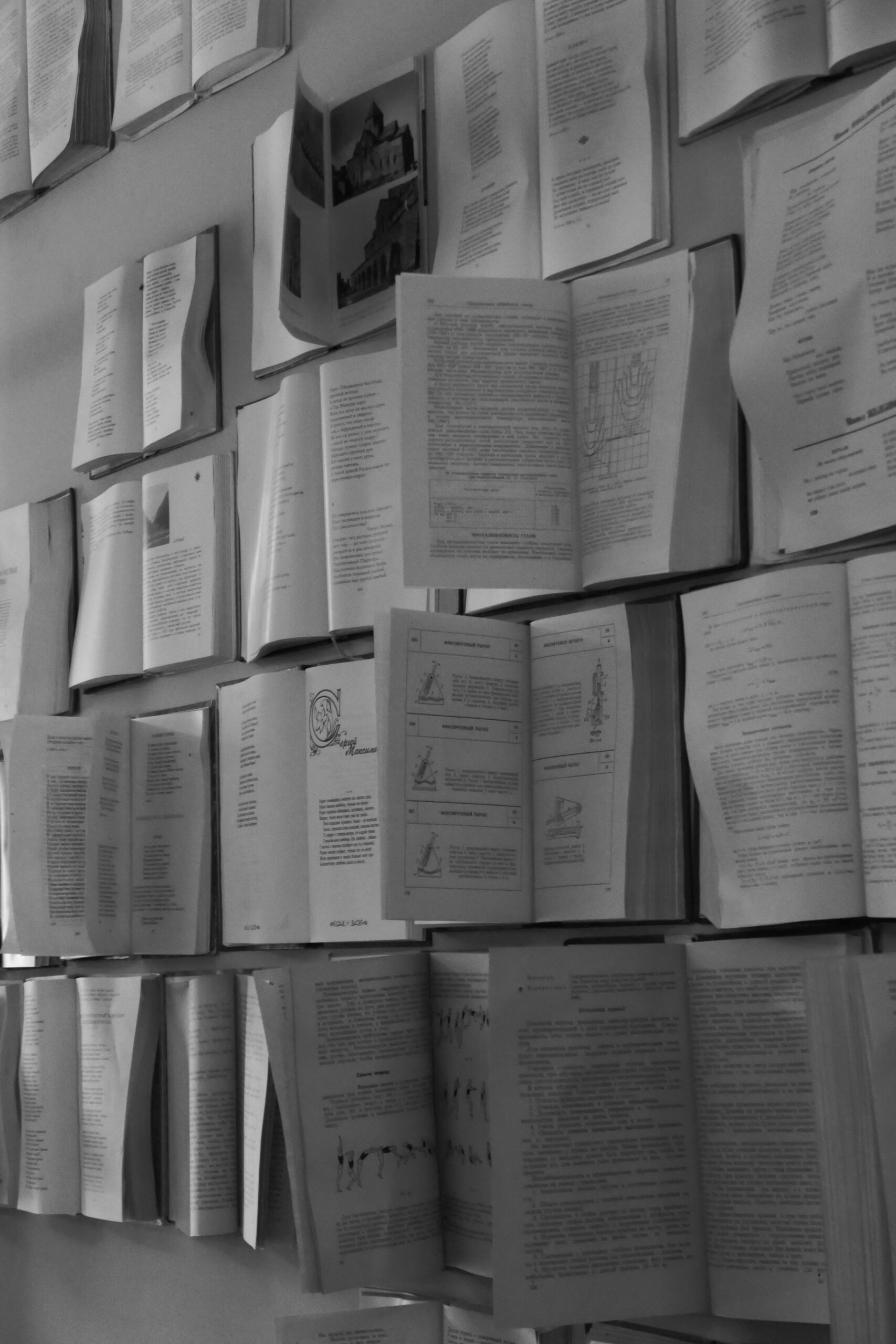 Vertical arrangement of open books on a wall, showcasing varied printed text in black and white.